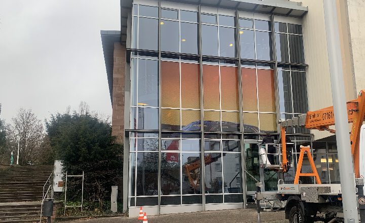 Die Stadthalle in Göppingen. Davor steht ein Hubsteiger mit dessen Hilfe das Wekr "GOLDEN" an der Glasfassade angebracht wird.