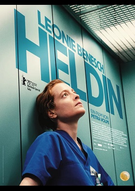 Filmplakat für den Film Heldin. Eine rothaarige Frau in einem blauen Ärztekittel lehnt mit leerem Blick an einer Aufzugswand.