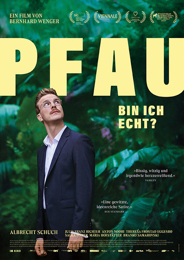 K3 Filmplakat: PFAU – Bin ich echt? Filmplakat zum Film „PFAU – Bin ich echt?“ zeigt einen jungen Mann im Anzug mit Brille, der nachdenklich nach oben blickt. Er steht vor einem üppigen, grünen Dschungelhintergrund. Der Titel „PFAU“ ist in großen, gelben Buchstaben oben zu sehen, darunter der Schriftzug „Bin ich echt?“ in Türkis. Oben sind mehrere Filmpreise und Festival-Logos abgebildet.