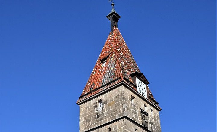 Spitzer, rot gedeckter Turm des mittelalterlichen Schmiedturms in Schwäbisch Gmünd vor strahlend blauem Himmel.