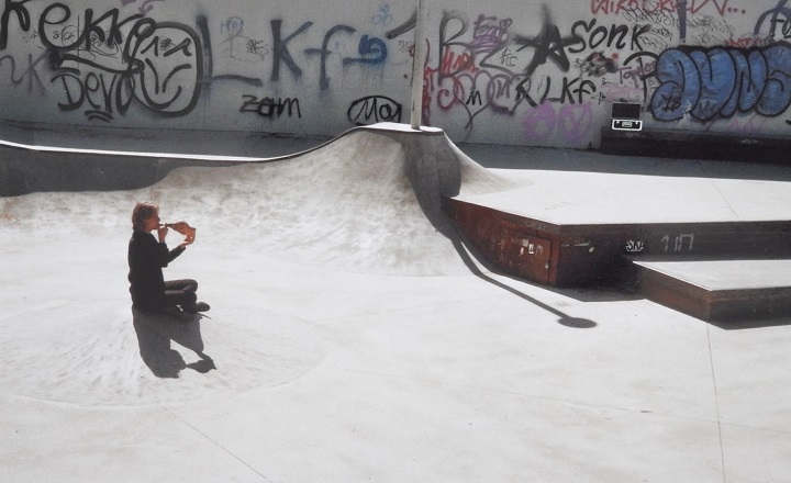 KATHLEEN JAHN. FREQUENZEN Kathleen Jahn sitzt im runden Betonbecken eines Skateparks und spielt auf einem Schneckenhorn. Sie ist von Graffiti umgeben, das Licht betont die Struktur des Bodens.