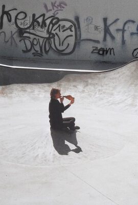 Kathleen Jahn sitzt im runden Betonbecken eines Skateparks und spielt auf einem Schneckenhorn. Sie ist von Graffiti umgeben, das Licht betont die Struktur des Bodens.