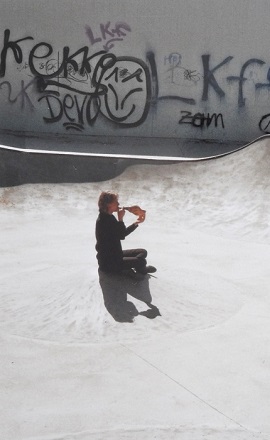 Kathleen Jahn sitzt im runden Betonbecken eines Skateparks und spielt auf einem Schneckenhorn. Sie ist von Graffiti umgeben, das Licht betont die Struktur des Bodens.