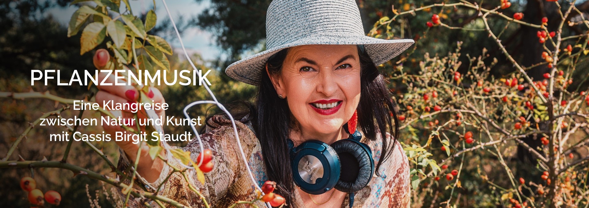 Cassis Birgit Staudt bei der Arbeit an ihrem Pflanzenmusik-Setup, zwischen Sträuchern mit roten Beeren, lächelnd in die Kamera.