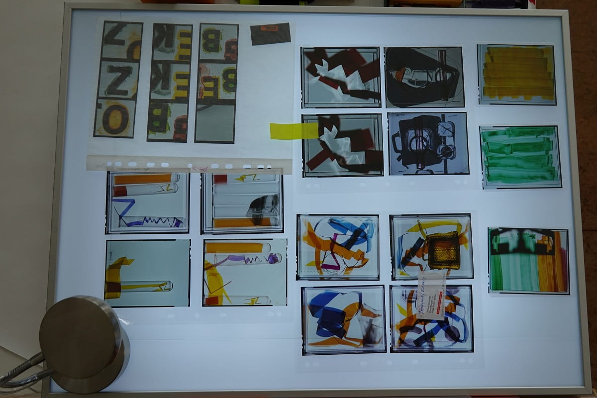 Auf einem Leuchttisch im Atelier von Simone Demandt liegen fotografische Entwürfe mit farbigen Linien, Formen, Buchstaben und gegenständlichen Motiven.