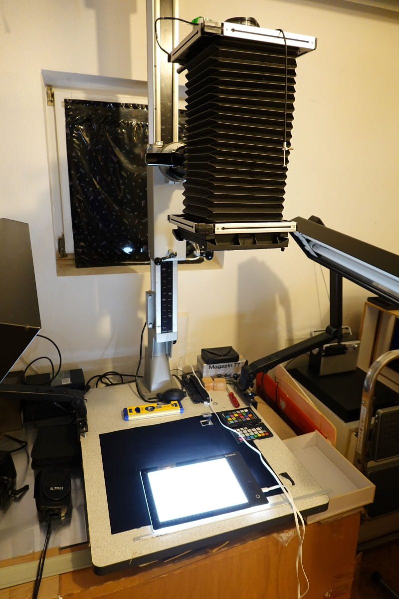 Eine große Fachkamera mit schwarzem Balgen steht im Atelier von Simone Demandt über einem beleuchteten Arbeitstisch mit Fototechnik und Farbtafeln.
