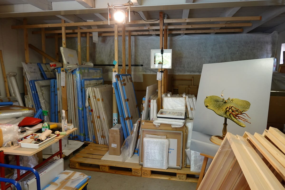 Lagerraum von Simone Demandt in Baden-Baden-Varnhalt mit verpackten Fotografien, Bilderrahmen, Arbeitsmaterialien und einem Objekt vor einer hellen Fotowand.